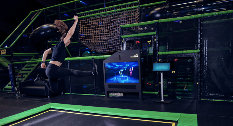 Mädchen springt in einer Pose hoch vor einem Bildschirm, auf dem ein Spiel läuft