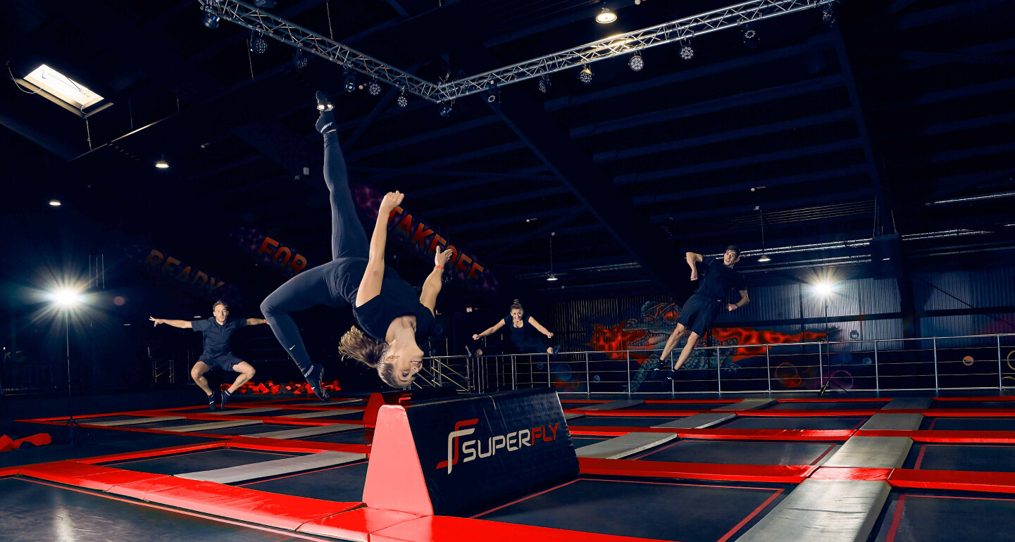 Personen machen Tricks auf einer roten Trampolinfläche